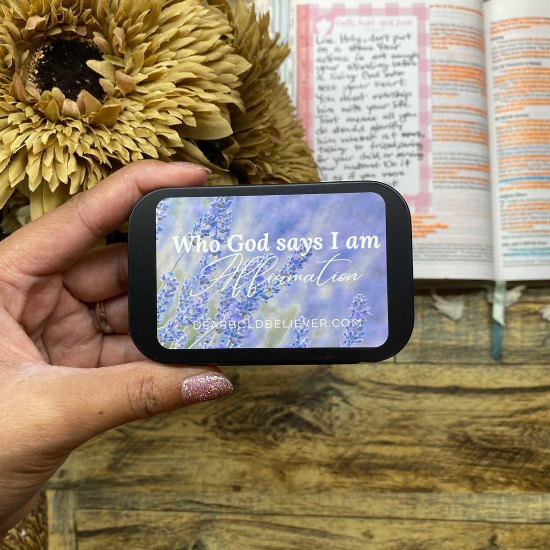 Hand holding a small bible verse cards tin with an open book and sunflower.