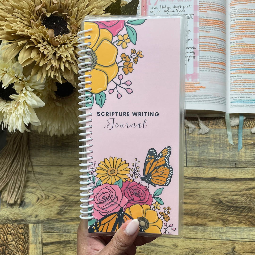 Hand holding a floral notebook with an open book and flowers on a wooden surface
