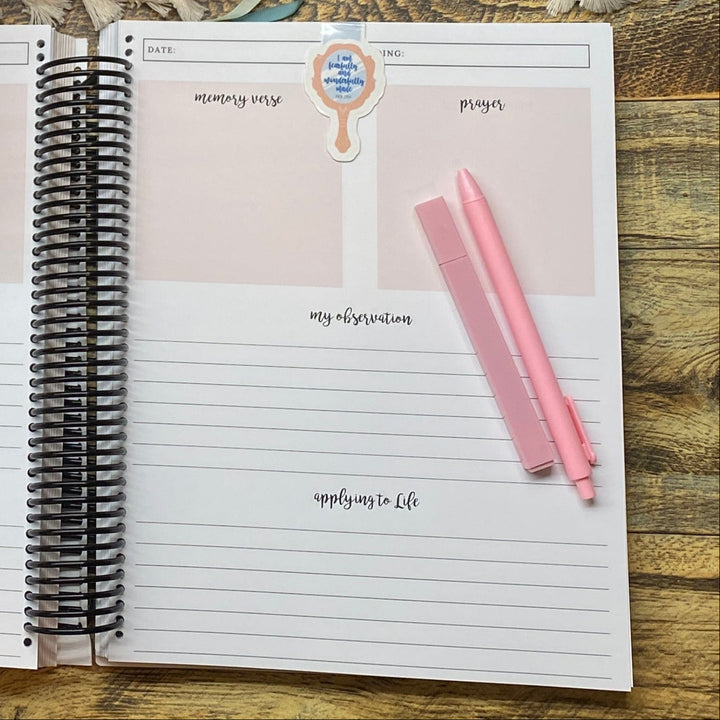 Open bible study notebook with pen, and flowers on a wooden desk