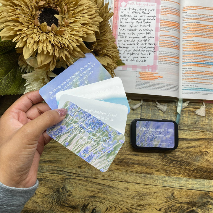 Hand holding scenic cards with an open book and sunflower in the background