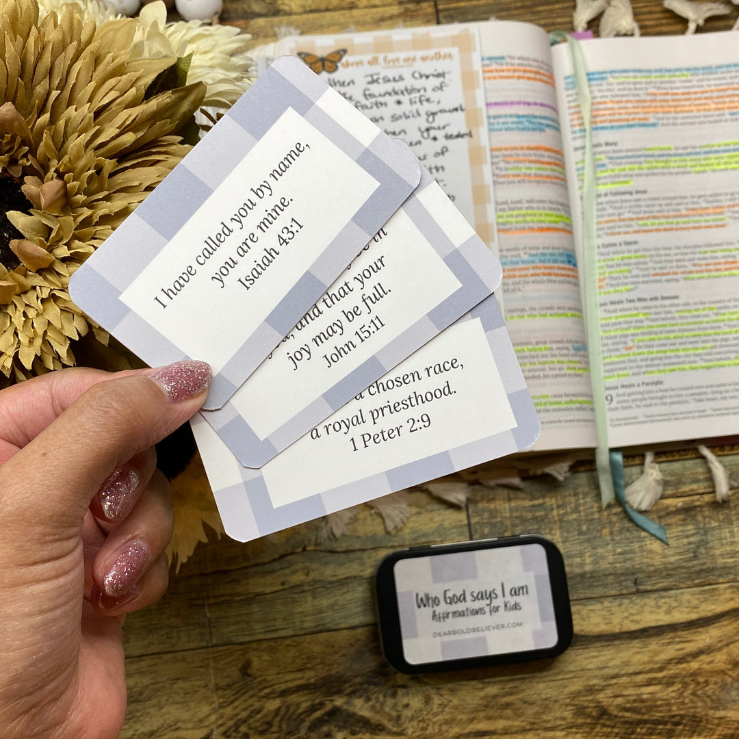 Hand holding a bible verse card with text over an open bible on a wooden surface.