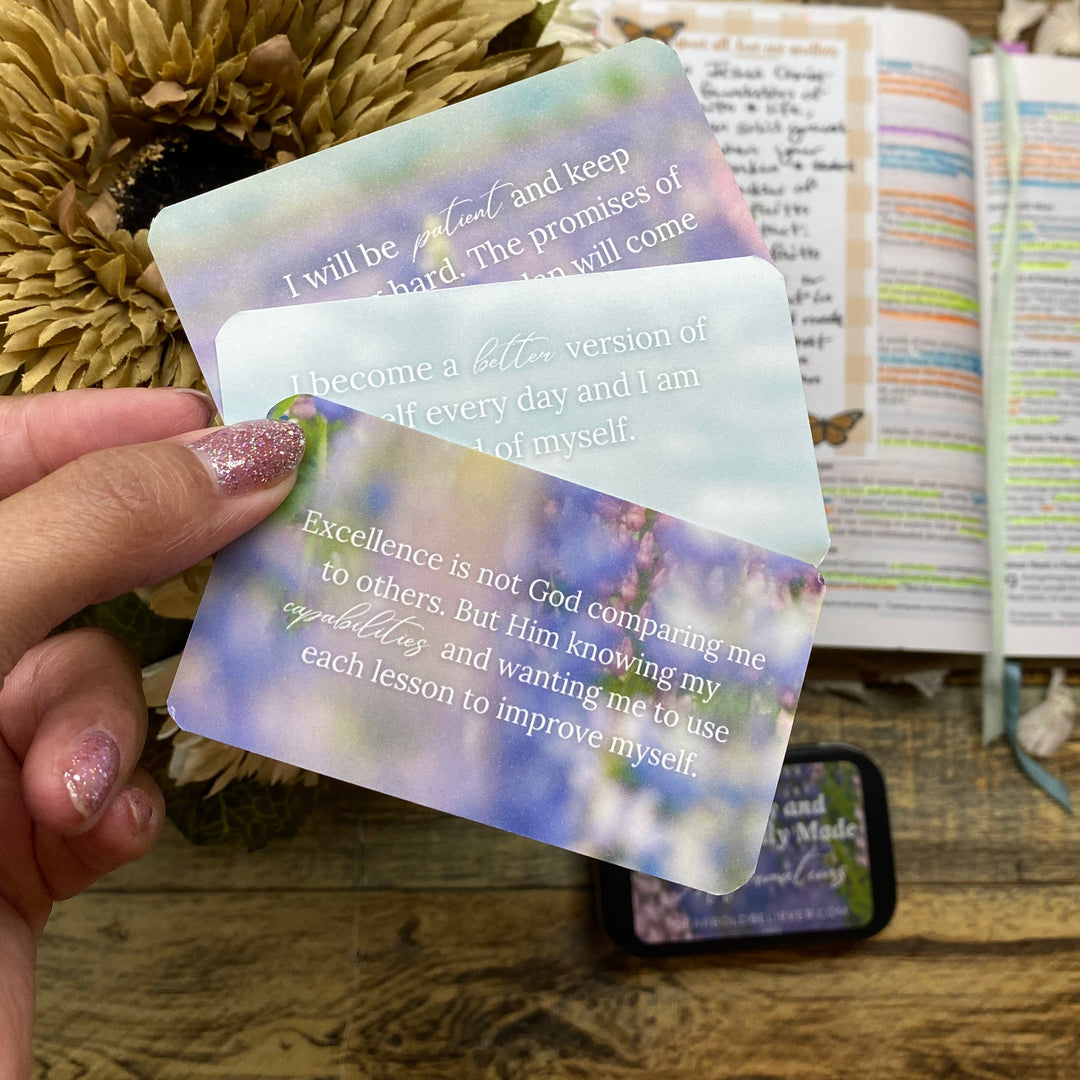 Hand holding a colorful scripture card with text, blurred background with bible and flowers
