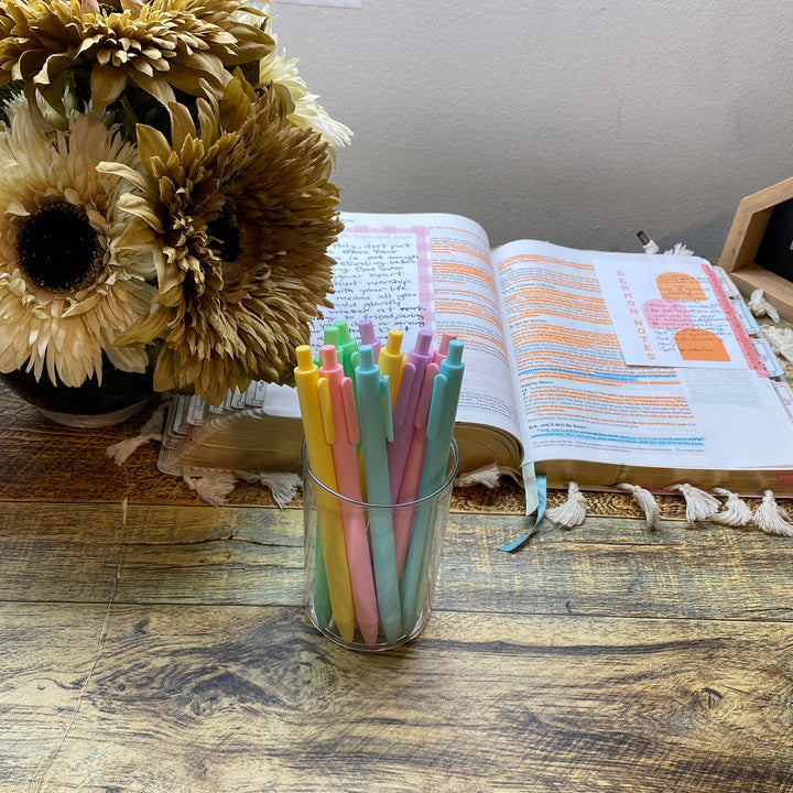 Colorful pens in a glass on a wooden table with an open bible and sunflowers.