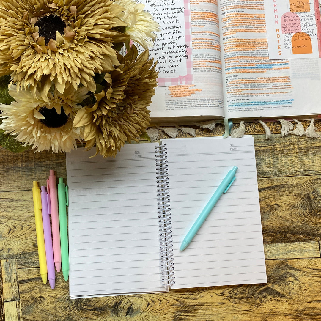 Open notebook with pen, flowers, and planner on a wooden desk