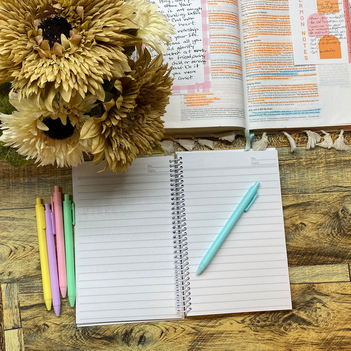 Open notebook with pen, flowers, and planner on a wooden desk