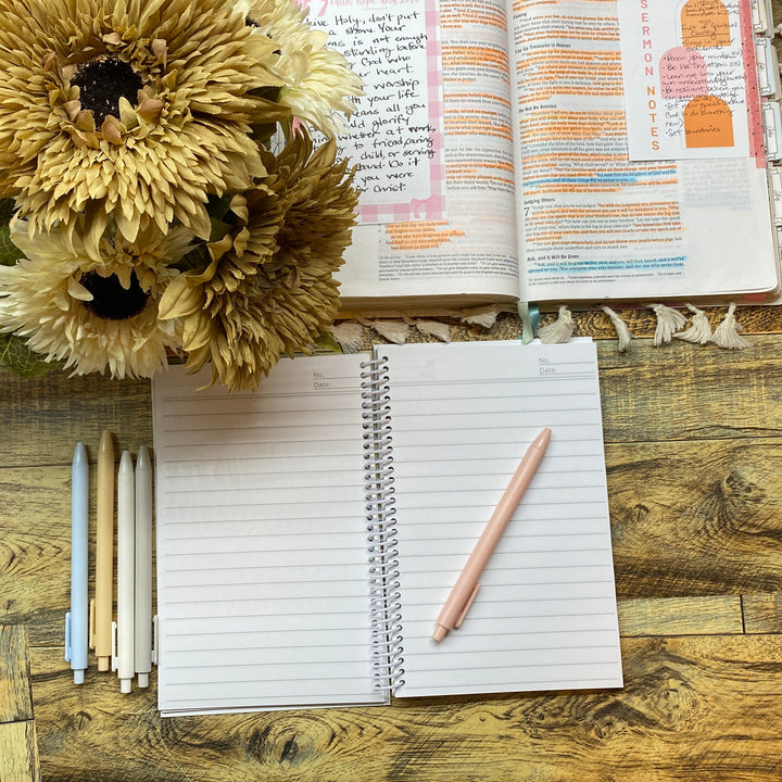 Open notebook with pen, flowers, and planner on a wooden desk