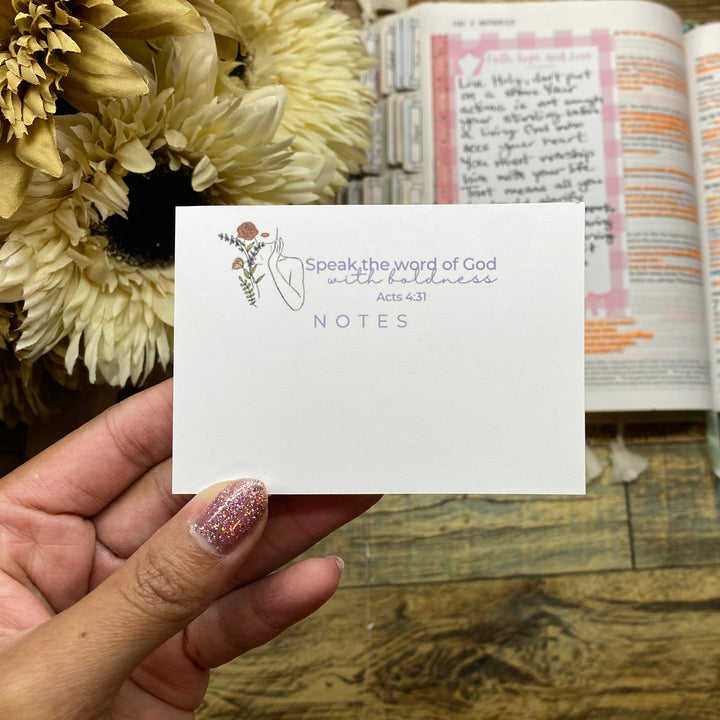 Hand holding a card with 'Speak the word of God' text over an open book on a wooden surface.