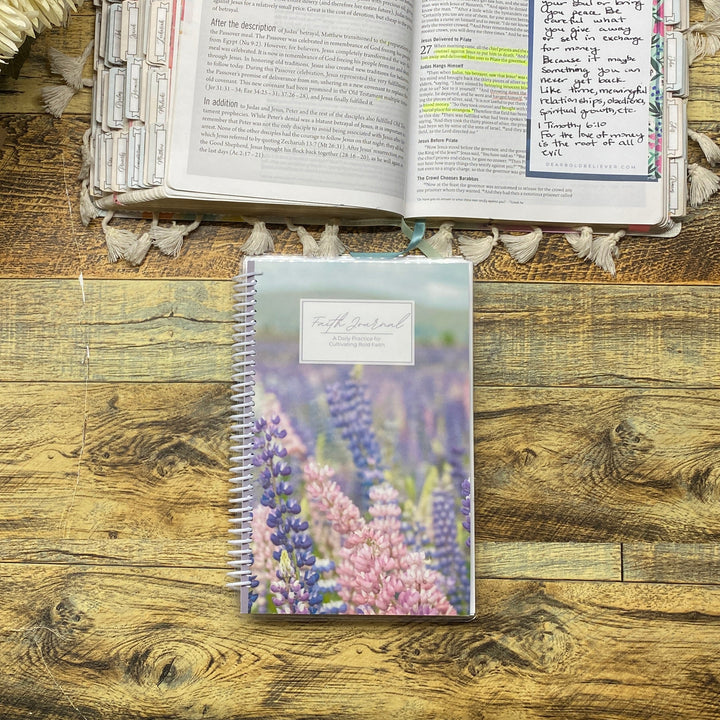 Open book with floral decorations on a wooden surface, next to a spiral-bound bible study journal.