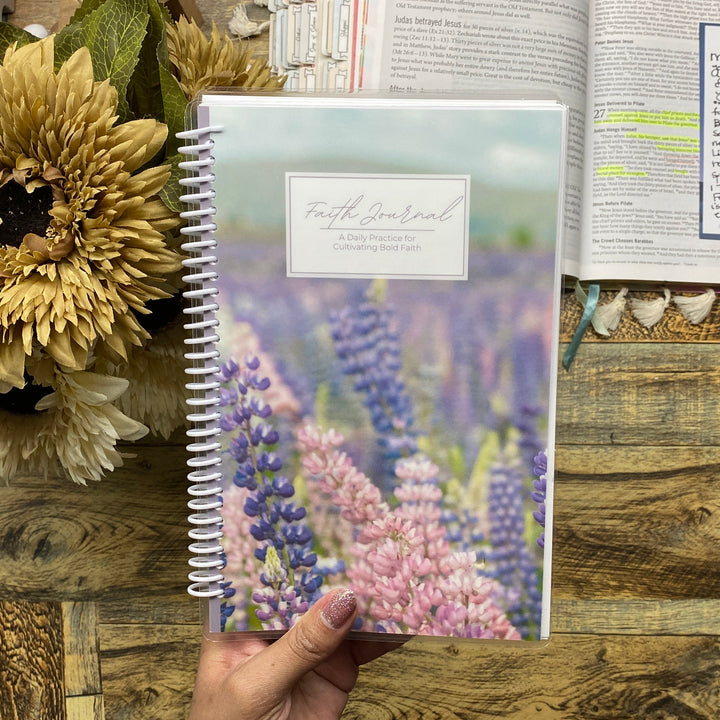Hand holding a notebook with floral design on a wooden surface with an open book and sunflower.