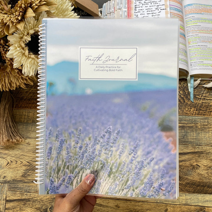Hand holding a spiral-bound bible study notebook with a lavender field design on a wooden table.