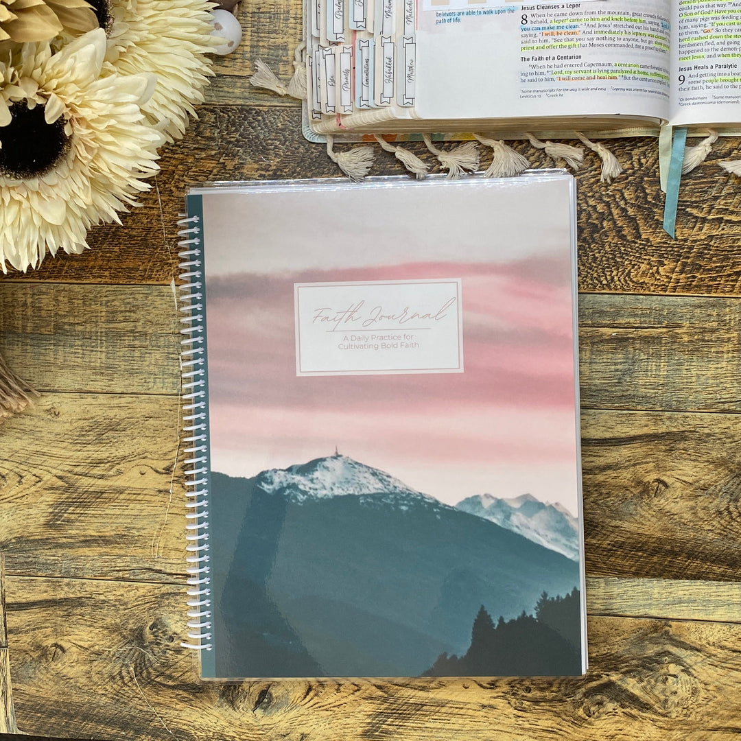 Notebook with mountain design on a wooden desk with flowers and stationery items.