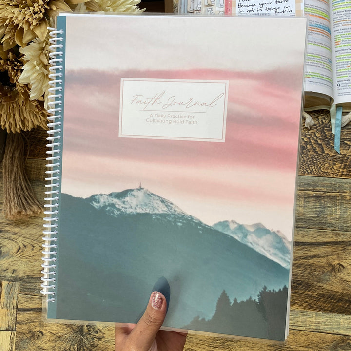 Person holding a spiral-bound notebook with mountain design on a wooden desk.