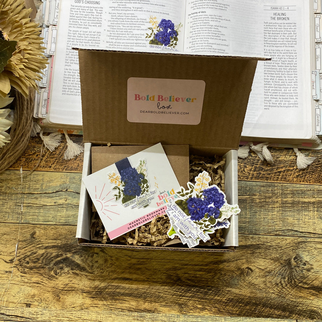 Box with decorative items on a wooden surface next to an open bible and flowers
