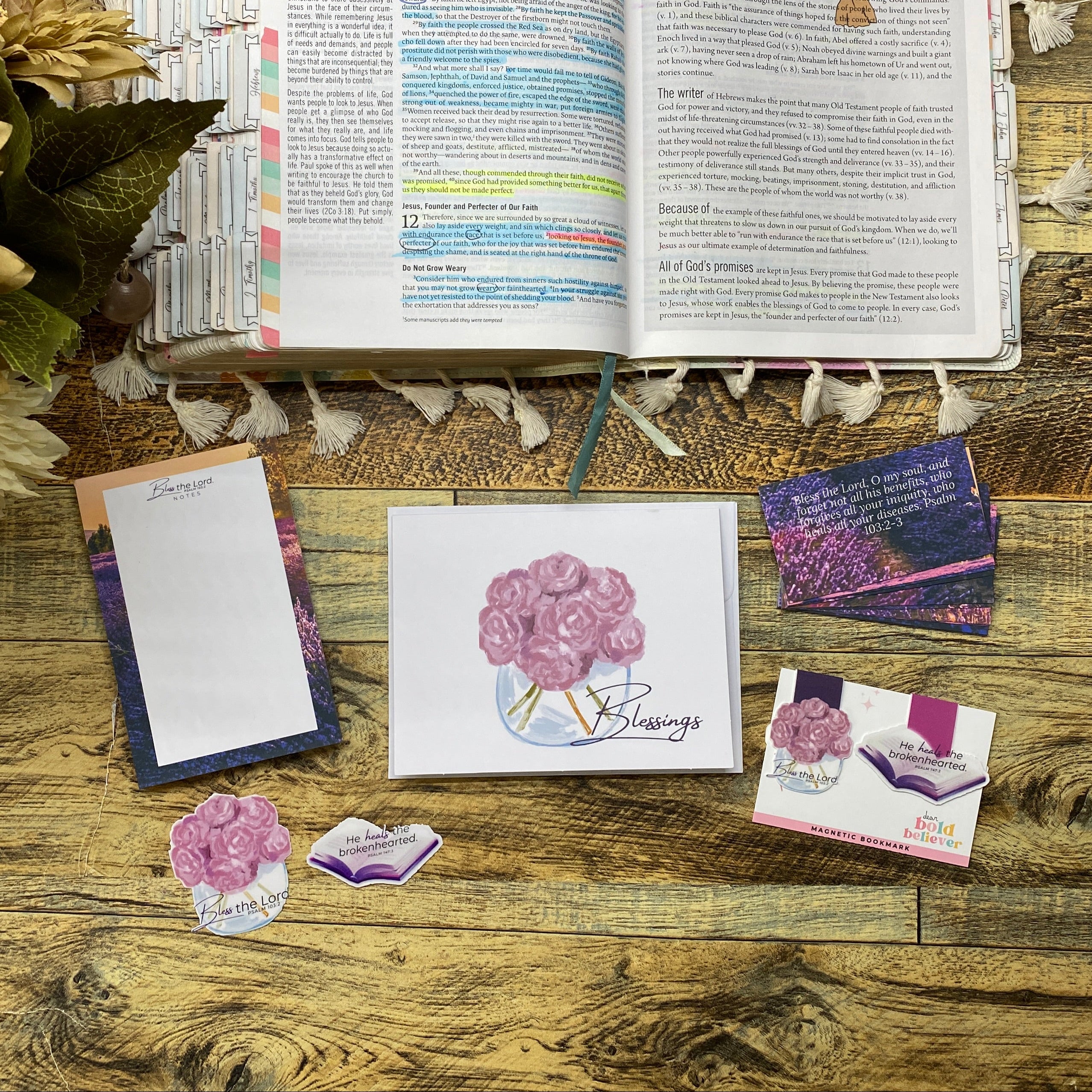 Open book with colorful text on a wooden surface, surrounded by decorative items like flowers and cards.