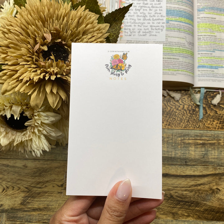 Hand holding a white card with a floral design, sunflowers, and an open book on a wooden surface.