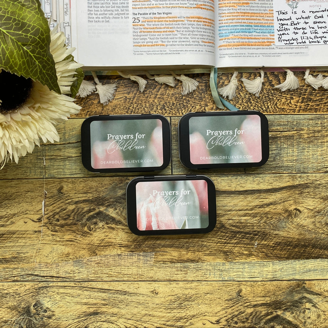Three prayer cards on a wooden surface with an open book and flowers in the background