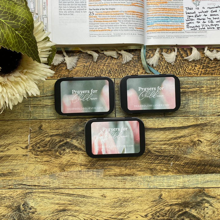 Three prayer cards on a wooden surface with an open book and flowers in the background