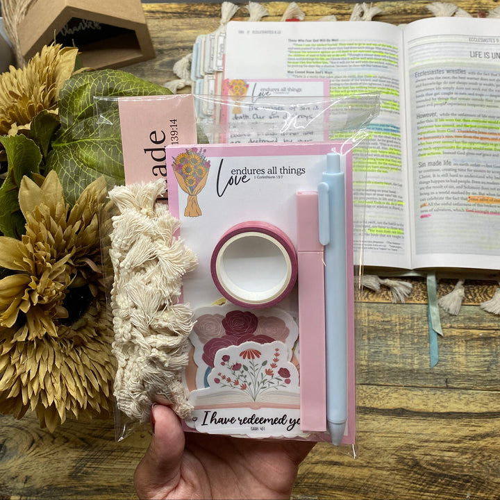 Hand holding a small book with a floral arrangement and open book in the background.