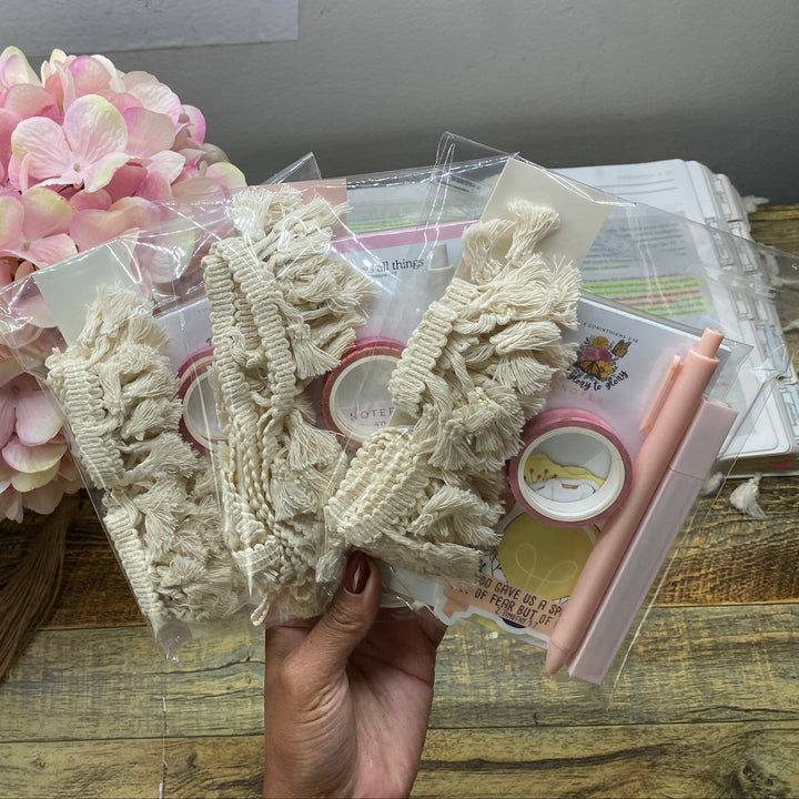 Hand holding lace trim with pink flowers and crafting materials in the background