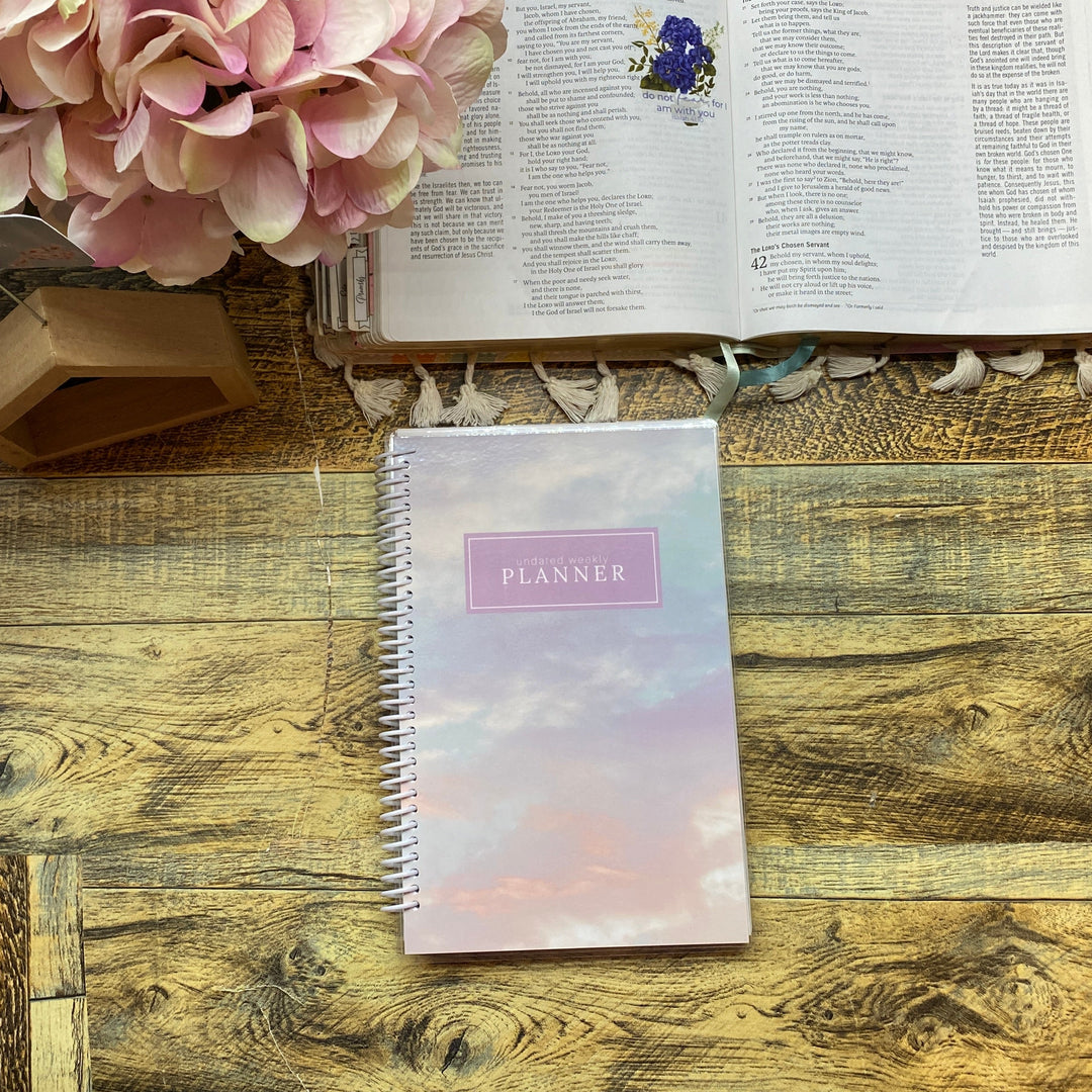 Open book with a planner and pink flowers on a wooden surface