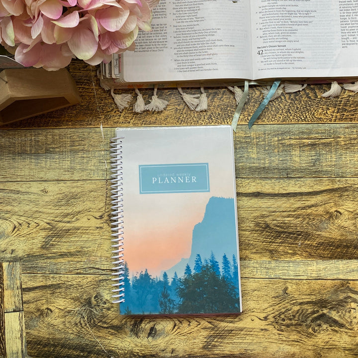 Open book with planner and pink flowers on a wooden surface