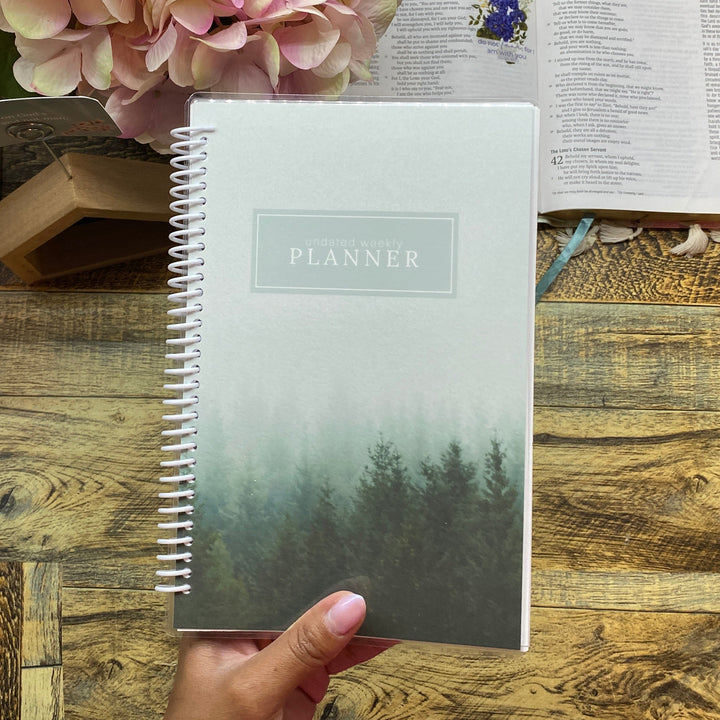 Planner on a wooden desk with flowers and an open book