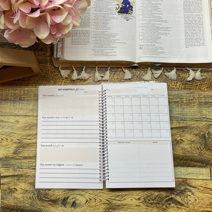Open book with a decorative flower on a wooden desk, next to a planner and printer.
