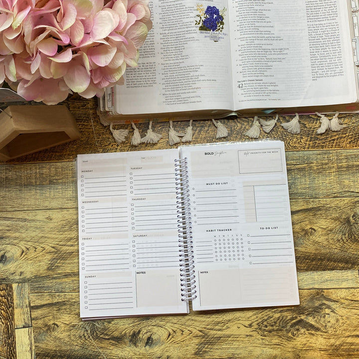 Open notebook and book on a wooden desk with pink flowers.