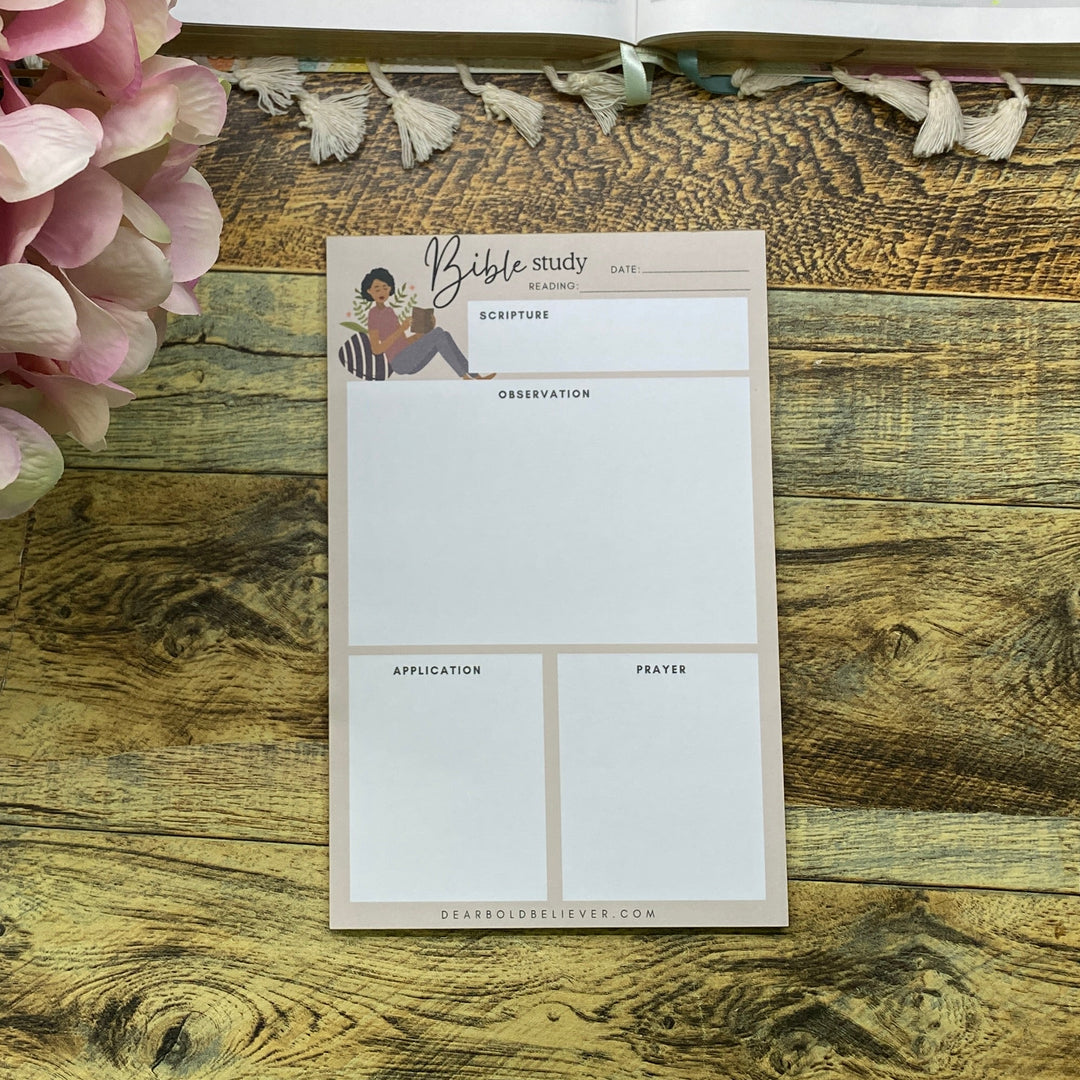 A styled flat-lay of a planner insert or postcard on a rustic wooden tabletop next to an open highlighter journal and a pink hydrangea flower.