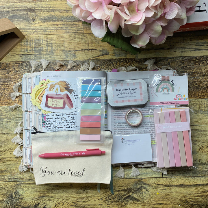 A styled flat-lay of a handmade planner or pocket organizer made from scrapbook paper, tape, and stickers, placed on a rustic wooden table next to pink hydrangeas.