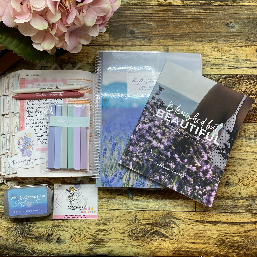 A styled flat-lay of stationery and notebooks on a rustic wooden table, featuring a spiral notebook with a cherry blossom cover, a clear plastic organizer, pastel sticky notes, a pink pen, and decorative flowers.