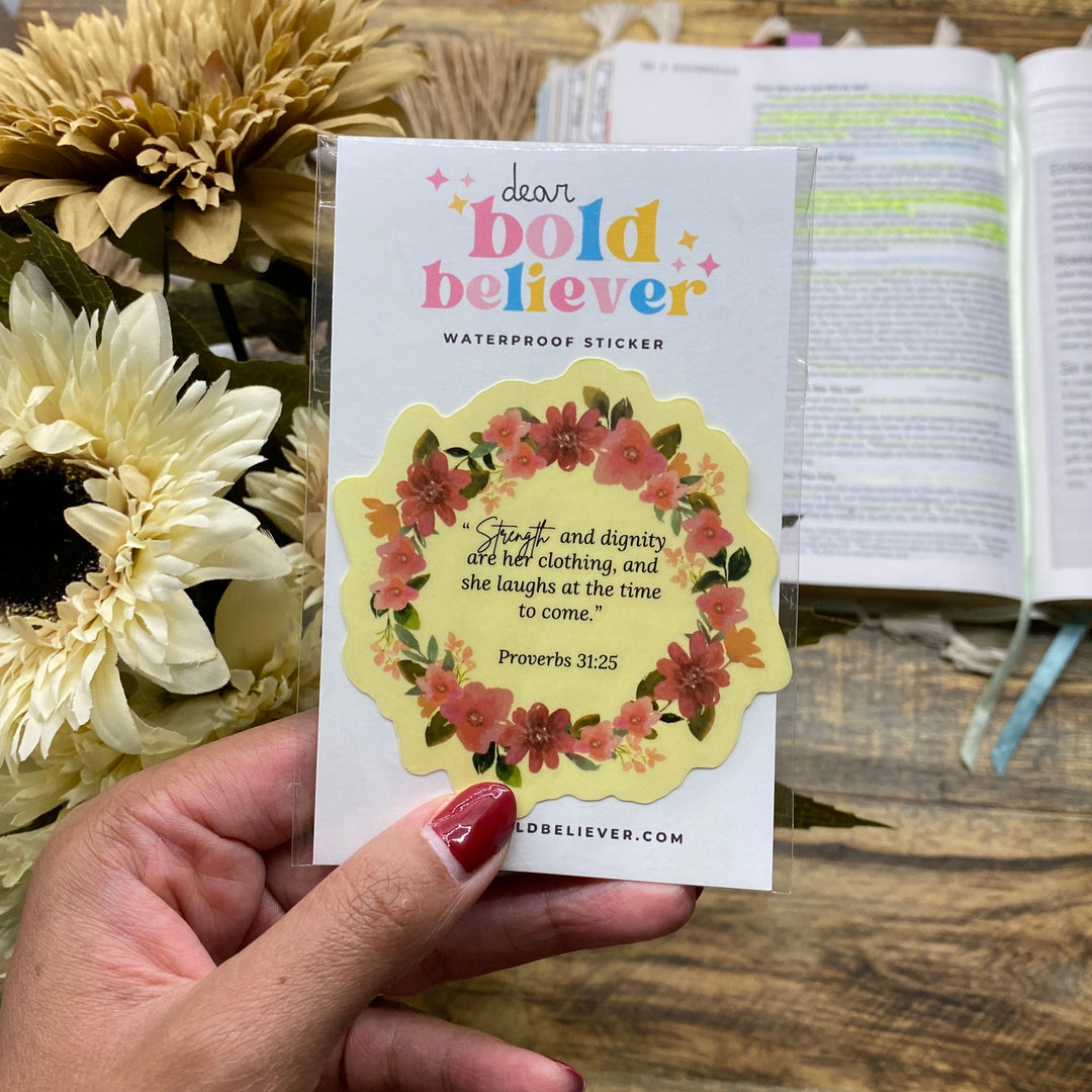 Hand holding a card with floral design and text, placed on a wooden surface with flowers.
